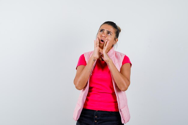 Woman holding hands near open mouth in t-shirt, vest and looking surprised