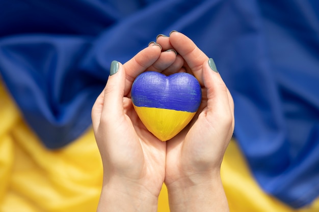 Free Photo woman holding heart with ukrainian flag over another flag