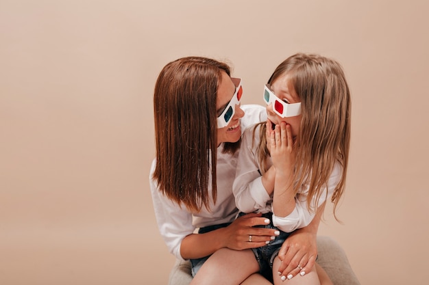 Woman holding her little charming girl and wearing glasses for cinema Little girl watching movie with her mother