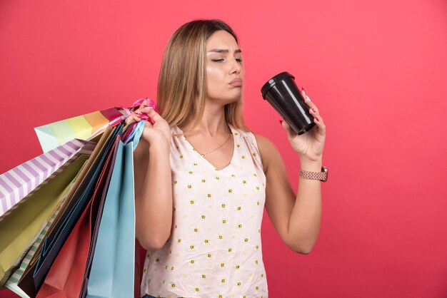 Woman holding her shopping bags and drinking cup of coffee .