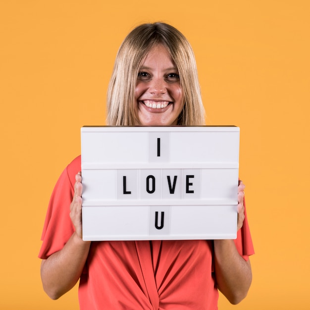 Woman holding light box with i love you text against plain studio backdrop