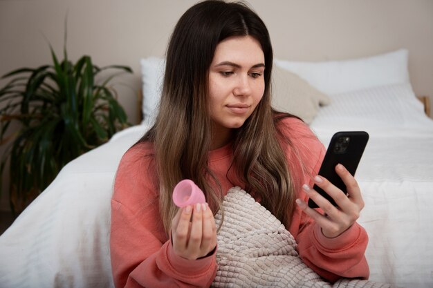 Woman holding menstrual cup and phone medium shot