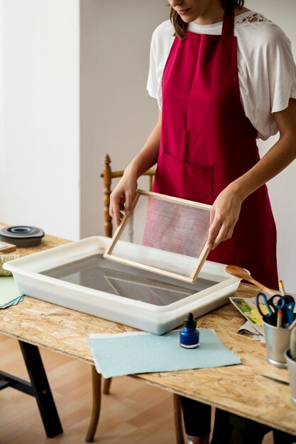 Woman holding mold over tray filled with paper pulp