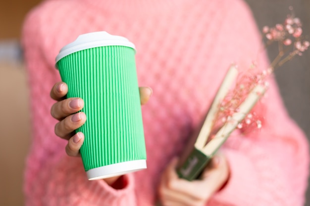 Free Photo woman holding an open book with a bouquet of dried flowers inside and a paper cup of coffee 