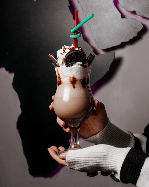 Woman holding oreo milkshake with whipped cream, chocolate syrup and cookies