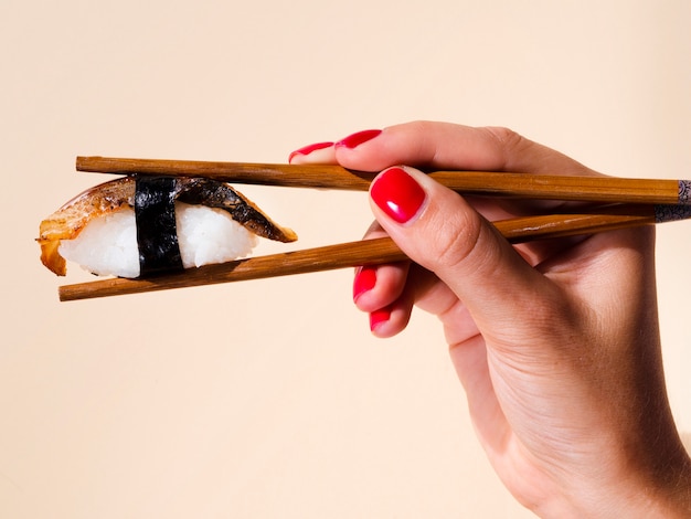 Free Photo woman holding in a pair of chopsticks a sushi on a pale rose background