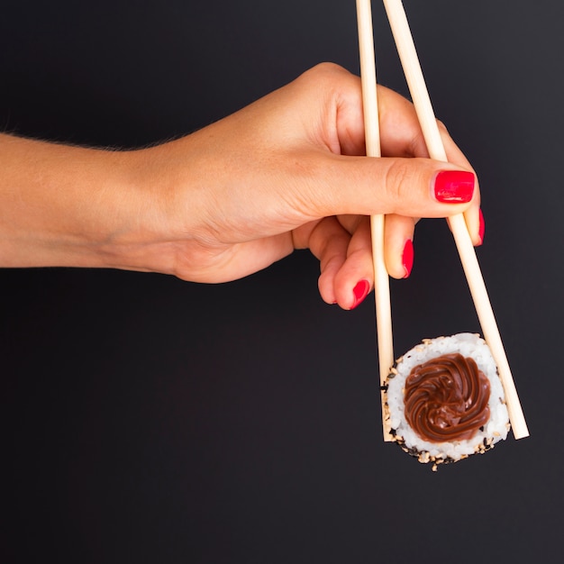 Free Photo woman holding a pair of chopsticks with a sushi roll on a black background