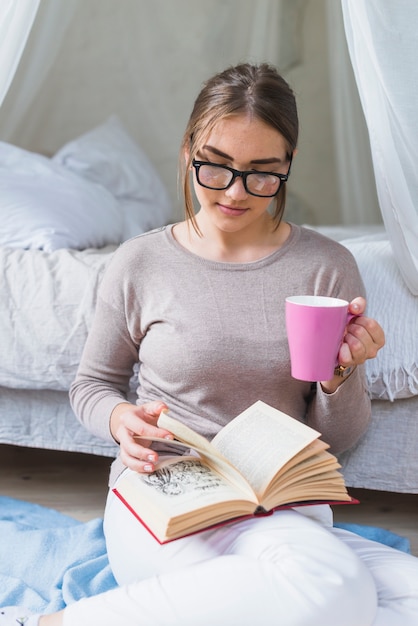 Woman holding pink coffee cup reading book in the bedroom