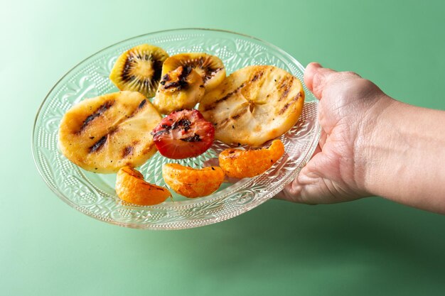 Woman holding a plate of grilled fruit on green background