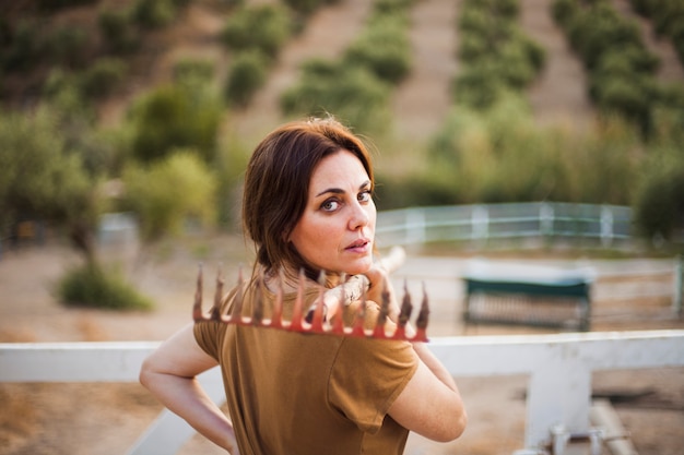 Free Photo woman holding rake on her shoulder standing in field