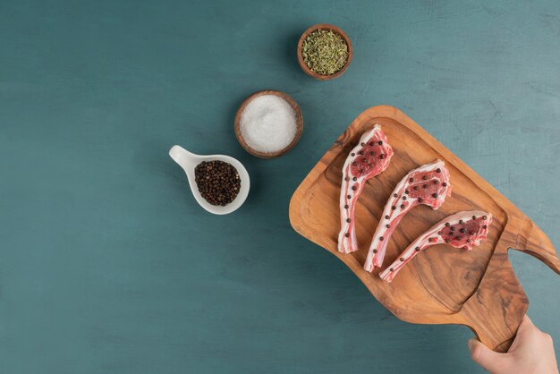 Woman holding raw meat wooden board on blue table.