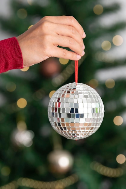 Free Photo woman holding silver christmas disco ball on christmas tree background