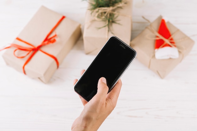 Woman holding smartphone above gift boxes