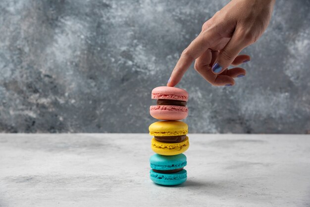 Woman holding stack of macarons on white table. 