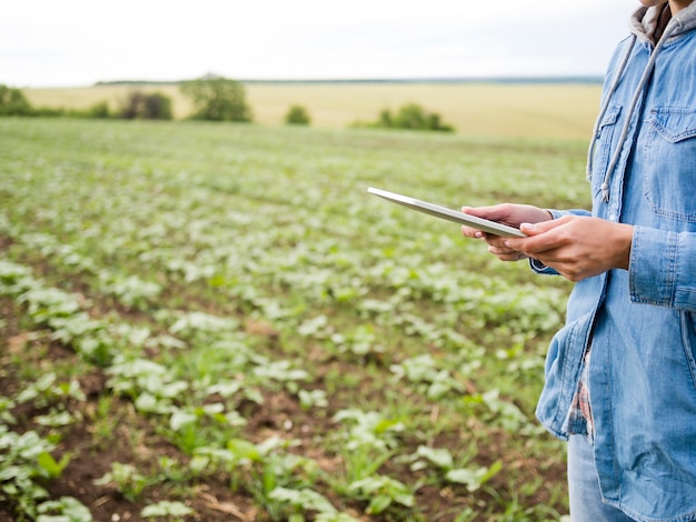 Free Photo woman holding a tablet next to a farm field with copy space