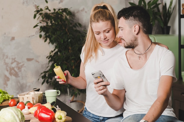 Woman holding vegetable in hand looking at cellphone hold by her boyfriend