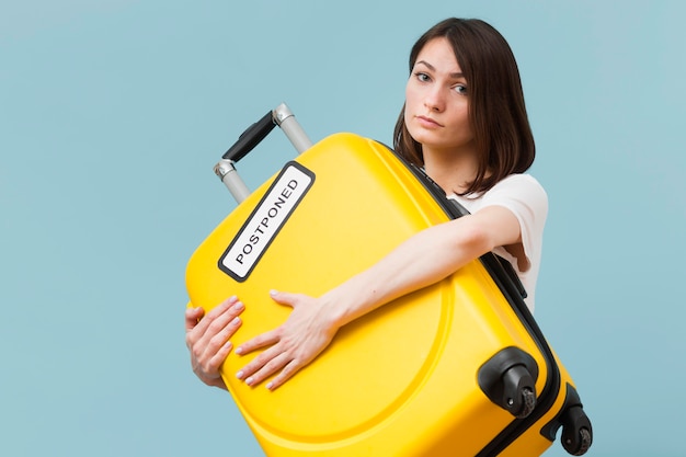 Woman holding a yellow baggage with a postponed sign