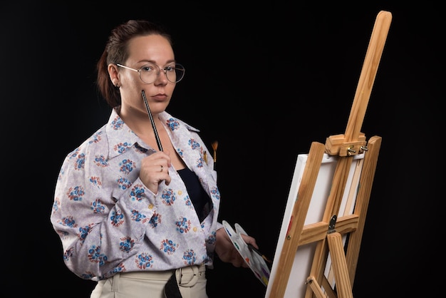 Woman holds brush and paints on black