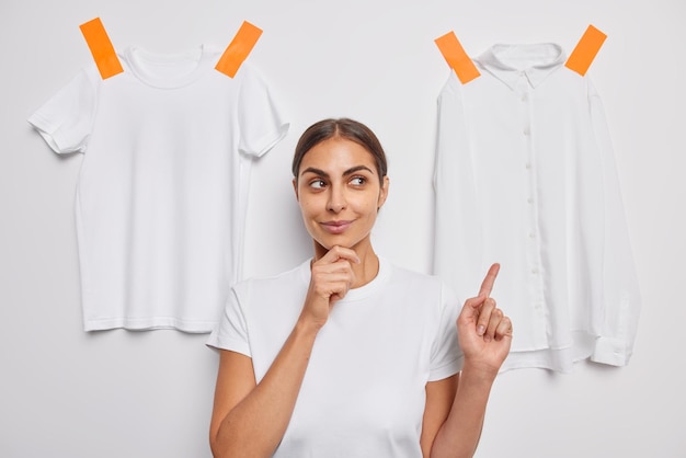 Free Photo woman holds chin indicates at items of clothing dressed in casual t shirt poses on white