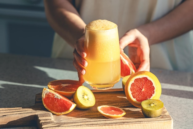 Free photo a woman holds a glass of freshly squeezed juice in her hands in the kitchen