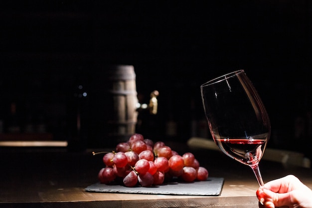 Woman holds glass of wine before bunch of grape lying on black plate