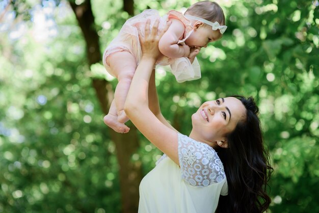 Woman holds her little daughter up standing in a green forest