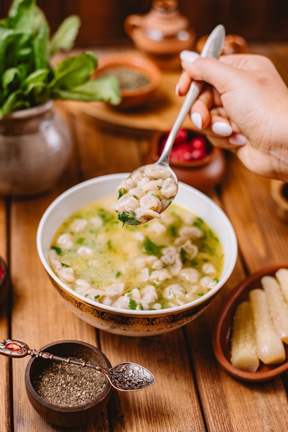 Free Photo woman holds a spoon of dushbara dumpling soup served with dried herbs and spices