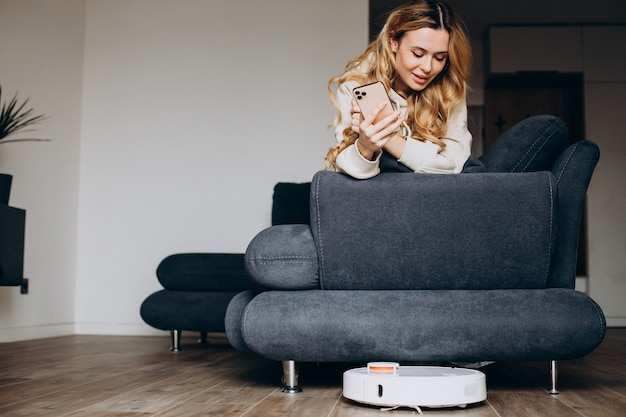 Woman at home watching robot vacuum cleaner tiding the house