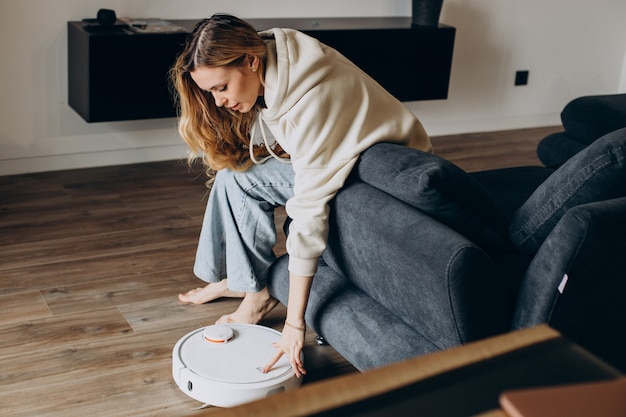 Free photo woman at home watching robot vacuum cleaner tiding the house