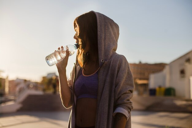 Woman in hoodie drinking water standing outside