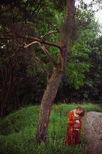 Free photo woman hugs her pregnant belly posing in the forest