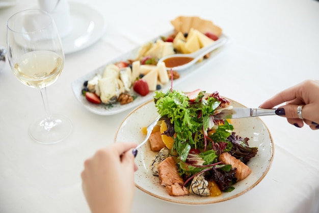 woman is eating pork salad with Lettuce, set cheese and a glass of wine