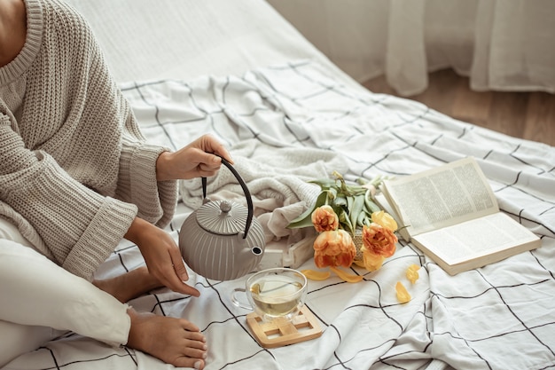 A woman is resting in bed with tea, a book and a bouquet of tulips