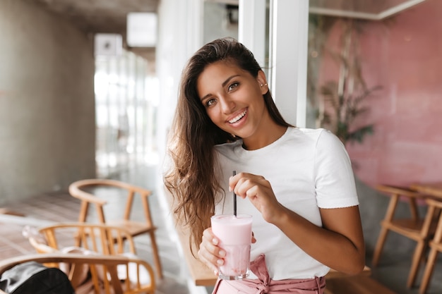 Woman is sitting in cozy cafe and stirring her strawberry smoothie