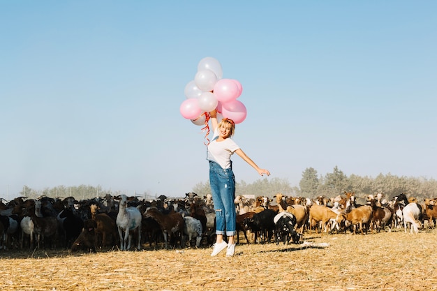 Woman jumping with balloons near goats