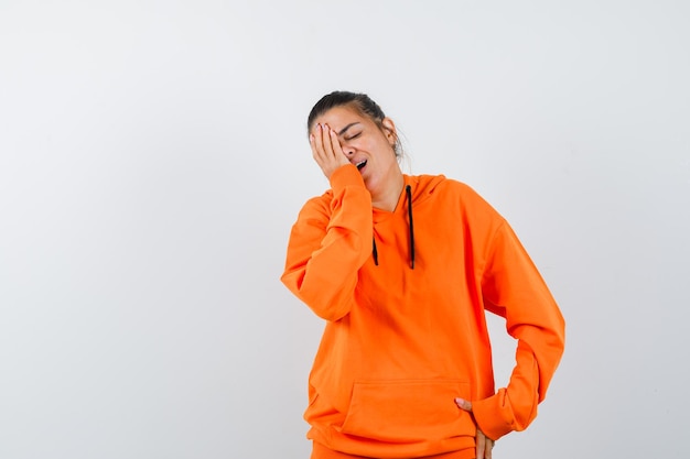 Woman keeping hand on face in orange hoodie and looking happy