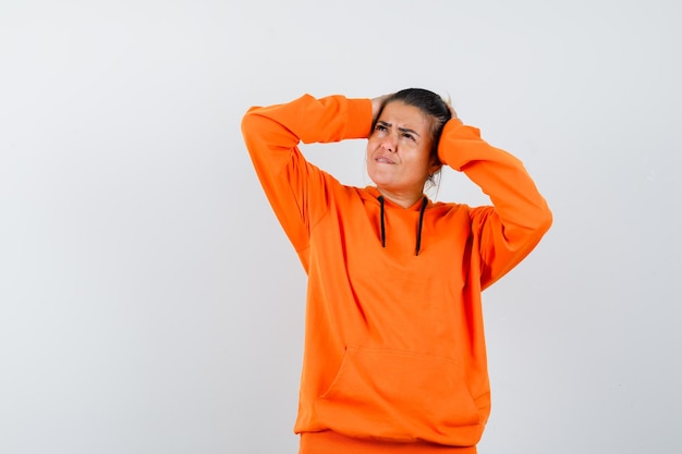 woman keeping hands on head in orange hoodie and looking forgetful