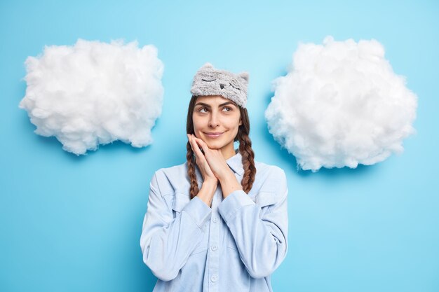 woman keeps hands near face concentrated above being deep in thoughts wears casual domestic clothes poses against blue 