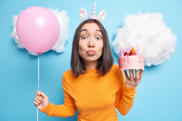 woman keeps lips folded enjoys holiday event holds delicious cake and inflated balloon celebrates 26th birthday makes wish