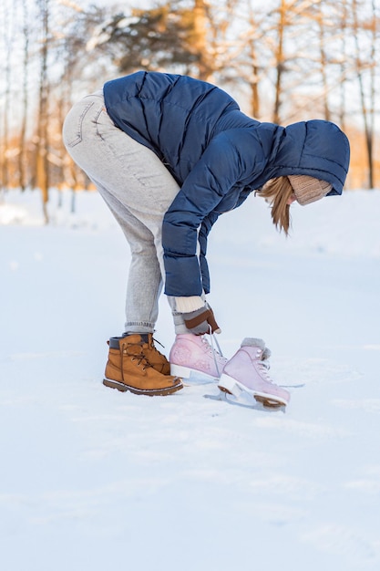 Free photo woman lacing ice skates at the edge of a frozen lake. cropped image of a woman putting ice skates on. winter sports, snow, winter fun