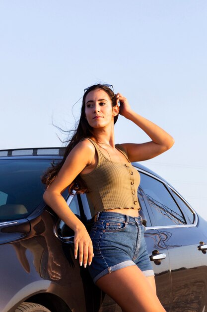 Woman leaning on car and posing in the sun