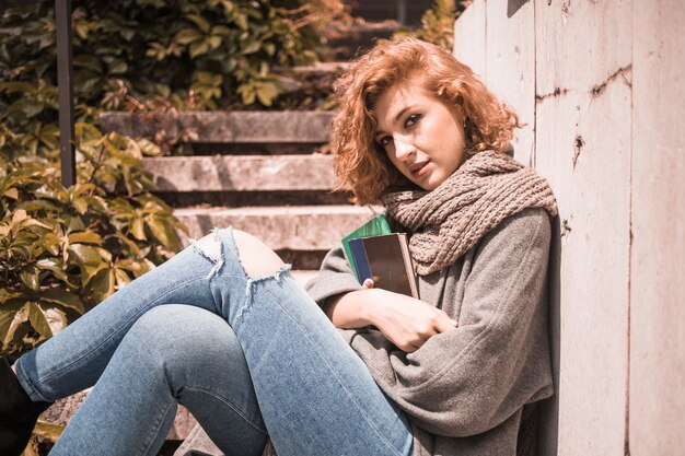 Woman leaning on wall and holding books 