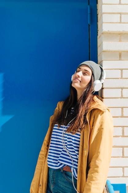 Free Photo woman leaning on wall wearing headphones with her eyes closed