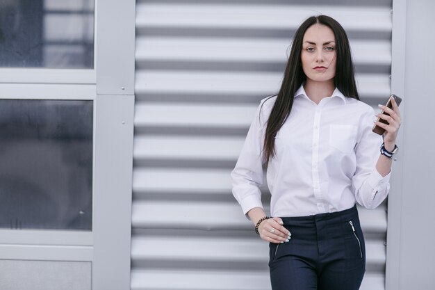 Woman leaning on a white wall with a phone in her hand