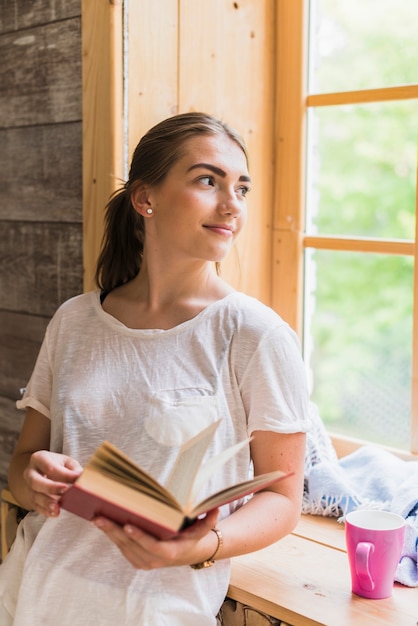 Woman leaning on window holding book in her hand