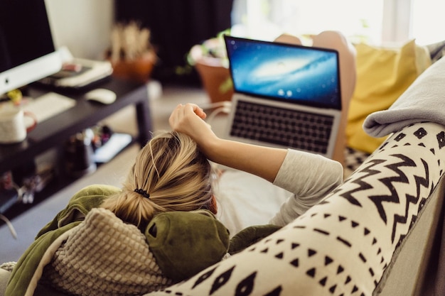 Free photo woman lies on a sofa with a laptop. leisure on isolation. working on a laptop from home.