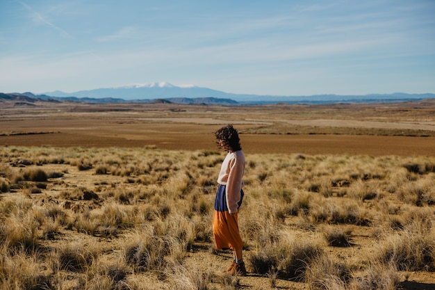 Free photo woman in a long sleeve sweater and a long skirt standing a large brownfield with dried grass