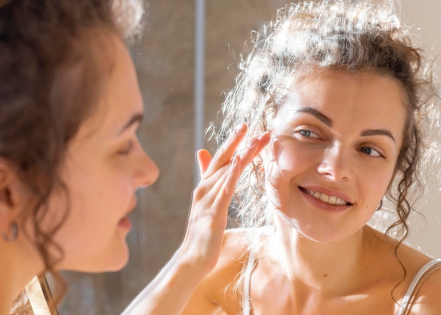 Free photo woman looking in mirror and applying face cream