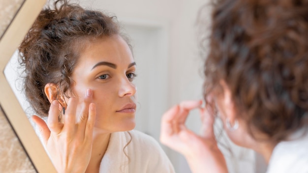 Free Photo woman looking in mirror and doing beauty face routine