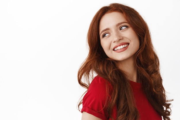 Free photo woman, looking behind shoulder carefree, smiling and gazing with thoughtful romantic smile, standing in t-shirt on white